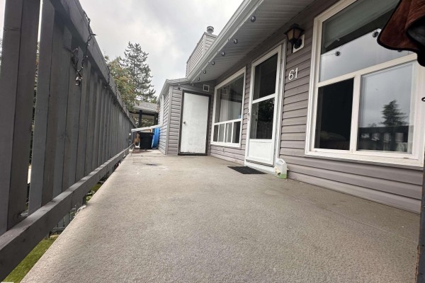 A concrete patio with a grey wooden fence and large windows on the exterior of a townhouse unit numbered 61. - #61 1503 Mill Woods Nw, Edmonton