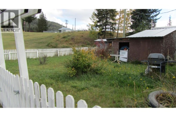 Backyard view with a shed, lawn, trees, and a distant hillside. - 61 375 Horse Lake Road, 100 Mile House