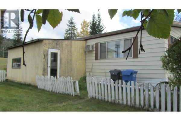 Side of mobile home and attached shed with white picket fence and trash bins. - 61 375 Horse Lake Road, 100 Mile House