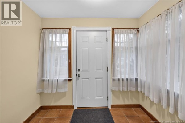 Interior view of a small entryway with a white door, tan walls, and two windows with sheer curtains. - 61-63 Burlington Avenue, Moncton