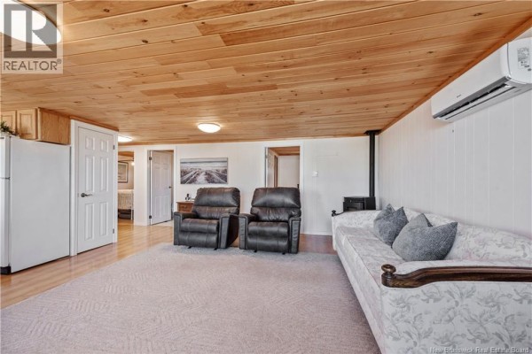 Living room with sofa, recliners, wood ceiling, and doors to other rooms and a refrigerator. - 61 Baybreeze Lane, Grand Barachois