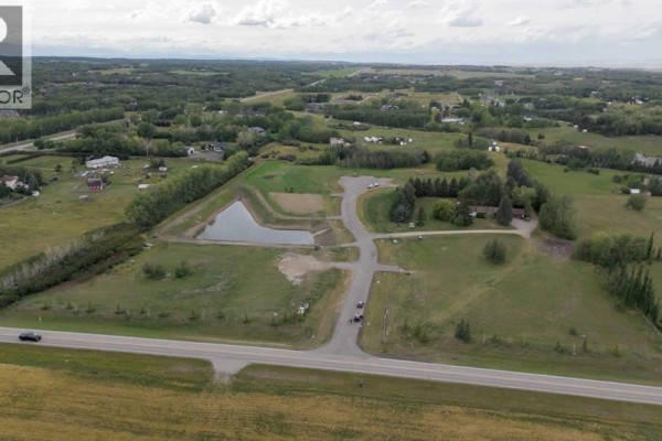 Aerial view of the rural landscape with multiple lots, roads, a pond, and distant homes. - 61 Bearspaw Heights Place, Rural Rocky View County