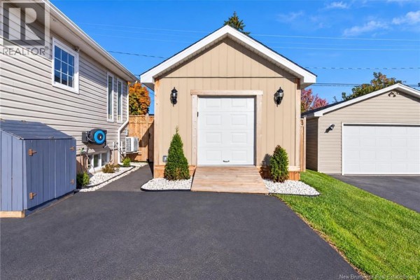 Side view of a beige vinyl-sided garage with a white overhead door and two small decorative evergreen trees. - 61 Bolton Street, Moncton