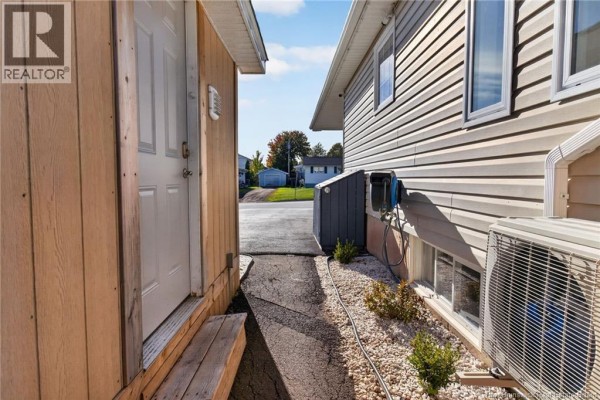 View between the bungalow and garage showing a paved walkway, outdoor AC unit, and storage shed. - 61 Bolton Street, Moncton