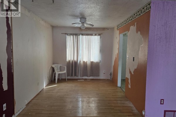 Bedroom with large window, peeling paint, and hardwood flooring. - 61 Chapman Street, Granisle