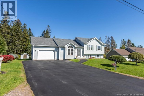 View of a light blue house with a garage and asphalt driveway on a sunny day. - 61 Fawcett Avenue, Sackville