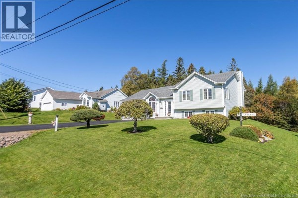 Side view of a light blue house on a grassy hill with trees and neighboring houses. - 61 Fawcett Avenue, Sackville