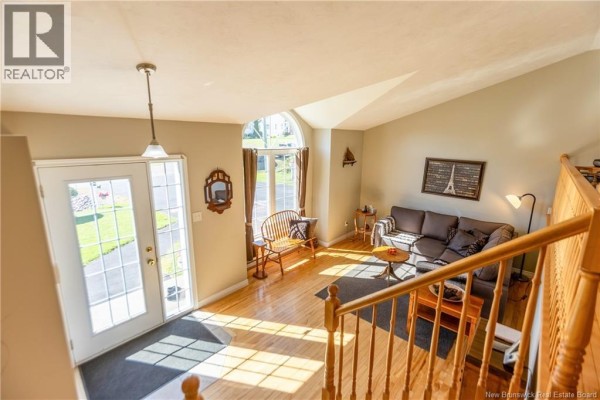 Living room with a vaulted ceiling, large arched window, gray sofa, and wood floors. - 61 Fawcett Avenue, Sackville