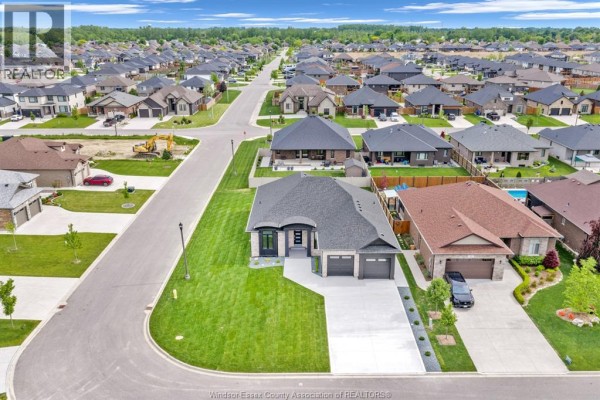 Front exterior of a beige brick bungalow with black trim, two garage doors, and a paved driveway. - 61 Hilton Court, Amherstburg