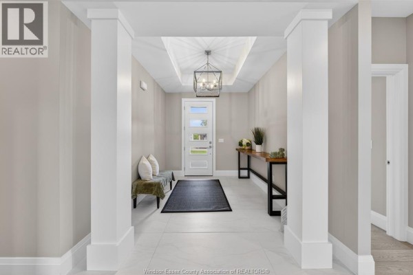 Staged foyer with gray tile floor, beige walls, a console table with decor, a bench, and artwork. - 61 Hilton Court, Amherstburg