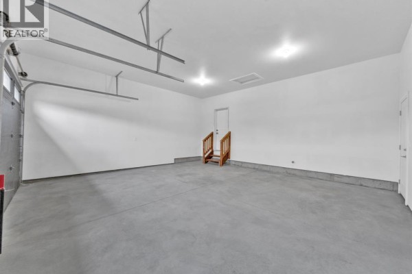 Spacious garage with concrete floor, white walls, overhead storage racks, and wooden stairs - 61 Hilton Court Amherstburg