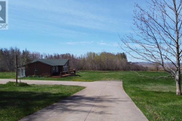 View of a brown house and detached garage from a concrete driveway on a sunny day. - 61 Shipyard Road, Cheverie