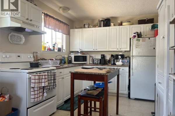 Kitchen interior showing white cabinets, refrigerator, stove, and a small island. - 61 View St, Nanaimo