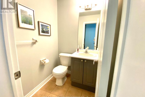 Powder room with toilet, vanity sink, gray cabinet, and framed artwork on wall. - 61 Walkerville Road, Markham