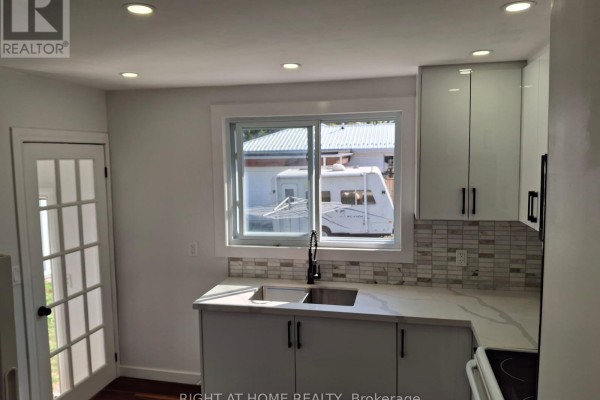 Kitchen with white cabinets, a window showing an RV, and a stainless steel sink. - 61 Wilkins Street, Quinte West