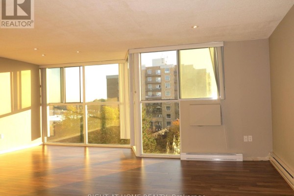 Living area with a white sofa, round coffee table, bookshelf, and a view into a white kitchen. - 610 - 127 Belmont Drive, London South