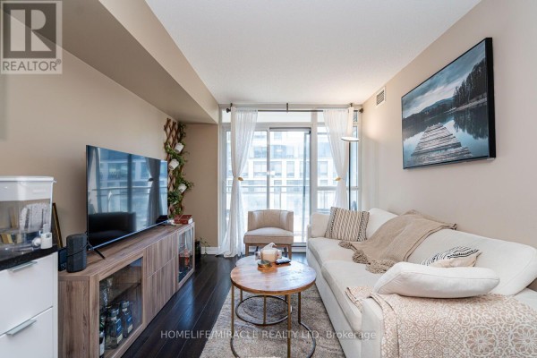 Living room with a white sofa, coffee table, television, and floor-to-ceiling windows. - 610 - 151 Dan Leckie Way, Toronto