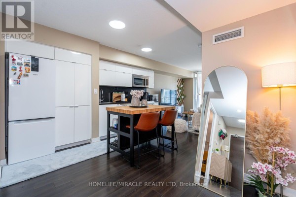 Kitchen area with white cabinets, a wooden island with bar stools, and stainless steel appliances. - 610 - 151 Dan Leckie Way, Toronto