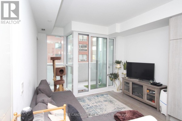 Living area with grey sofa, blue patterned rug, and sliding glass doors leading to a balcony. - 610 - 77 Mutual Street, Toronto