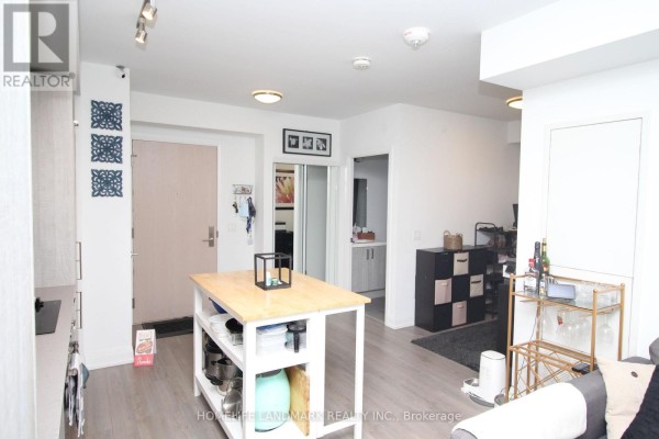 View from the kitchen island towards the apartment entrance, showing light wood floors and white walls. - 610 - 77 Mutual Street, Toronto