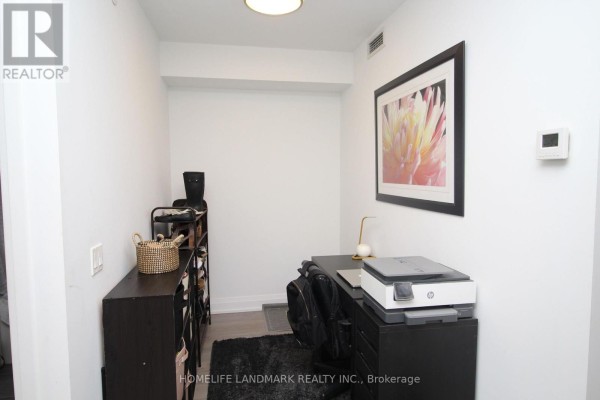 A small home office area with a black desk, chair, printer, and shelving unit against a white wall. - 610 - 77 Mutual Street, Toronto