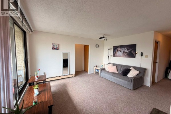 Living room with carpet, beige walls, grey sofa, and a large sliding glass door. - 610 1745 Leighton Rd, Victoria