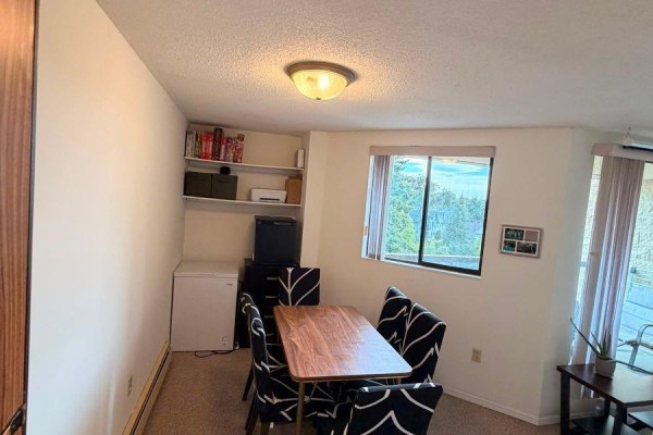 Dining area with a table, four chairs, shelves, and a window with a forest view. - 610 1745 Leighton Rd, Victoria