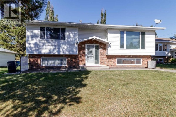 Front exterior of a split-level home with white siding and brick accents. - 610 8 Street N, Three Hills