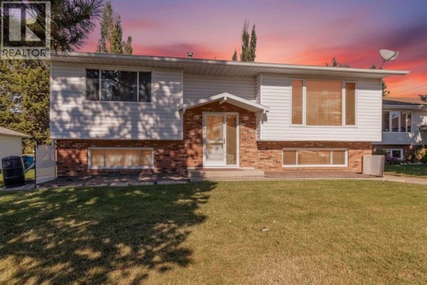 Front exterior of a split-level home with white siding and brick accents under a sunset sky. - 610 8 Street N, Three Hills