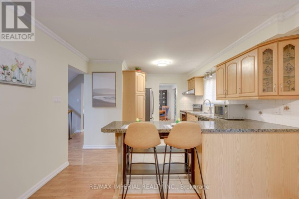 Kitchen with wood cabinets, granite island with bar stools, and stainless steel appliances. - 6100 Wabukayne Court, Mississauga
