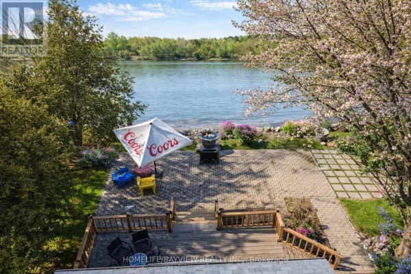 Deck and stone patio with umbrella, grill, and waterfront view. - 6108 Curtis Pt Road, Alderville First Nation