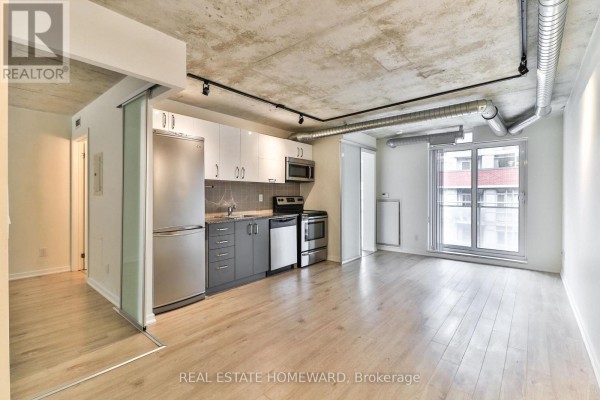 View of the living space and kitchen, with exposed concrete ceilings and sliding glass doors. - 611 - 170 Sudbury Street, Toronto