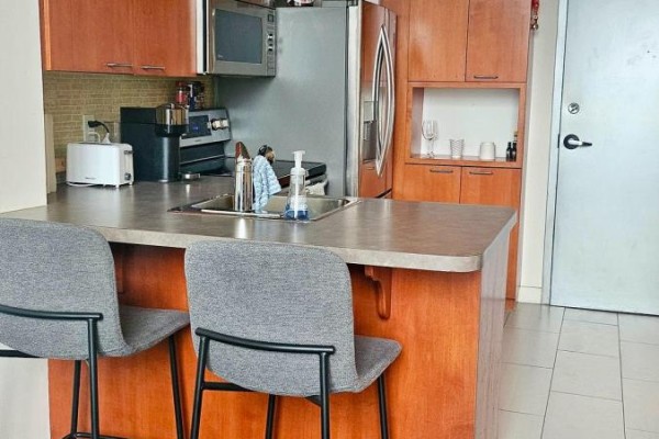 Kitchen island with two gray bar stools, light gray countertop, and wooden cabinets. - 611 - 255 Richmond Street E, Toronto