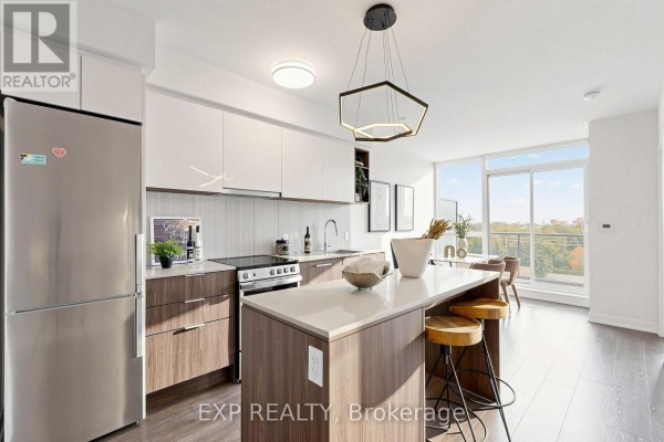 Modern kitchen with stainless steel appliances, island with seating, and large windows. - 611 - 31 Tippett Road, Toronto