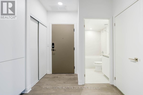 Apartment hallway with a neutral-toned door, closet, and bathroom entrance. - 611 - 4015 The Exchange, Mississauga