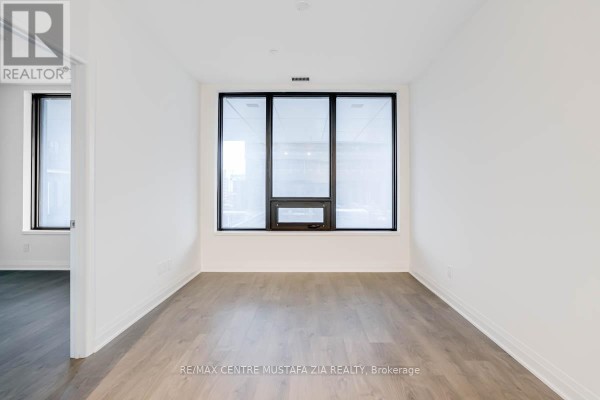Empty room with a large window overlooking city views and light wood flooring. - 611 - 4015 The Exchange, Mississauga