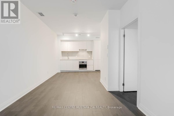 Bright open-concept living space with a modern white kitchen and grey wood flooring. - 611 - 4015 The Exchange, Mississauga