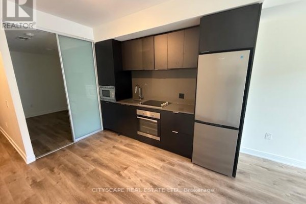 Compact kitchen with dark cabinets, stainless steel appliances, and light wood flooring. - 611 - 86 Dundas Street E, Mississauga