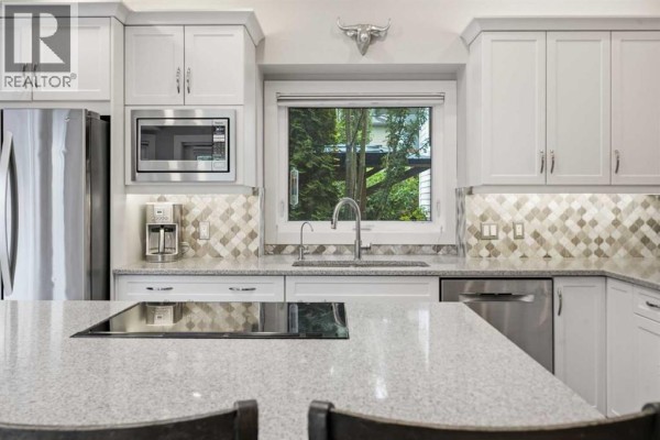 Close-up view of a white kitchen with granite countertops, stainless steel appliances, and a mosaic tile backsplash. - 611 25 Avenue Ne, Calgary