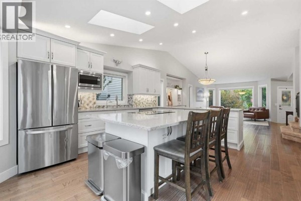 Spacious open-concept kitchen with white cabinetry, a large island with seating, and wood flooring. - 611 25 Avenue Ne, Calgary