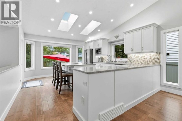 Bright kitchen with white cabinets, a large island, skylights, and a view of the backyard with a red umbrella. - 611 25 Avenue Ne, Calgary