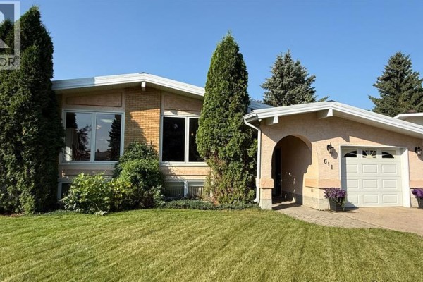 Front view of a single-story house with tan stucco, arched entryway, and attached garage. - 611 6 Avenue W, Hanna