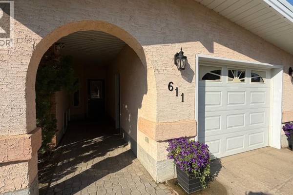 Arched entryway with paving stones, leading to dark teal front doors and an attached garage. - 611 6 Avenue W, Hanna