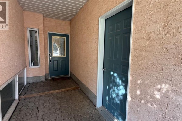 Covered walkway with two teal doors, a narrow window, and textured stucco walls. - 611 6 Avenue W, Hanna