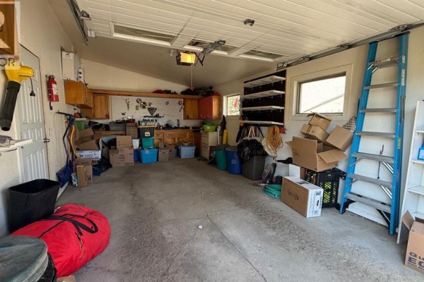 Interior of a two-car garage with concrete floor, storage shelves, wooden cabinets, and ladder. - 611 6 Avenue W, Hanna