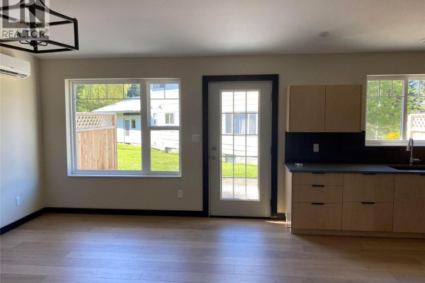 Living area with light wood laminate floors, large windows, a glass door, and light wood cabinets. - 611 Casley Court Unit# 2, New Denver