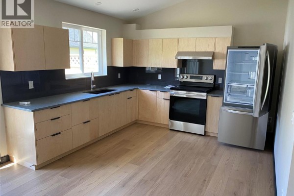 Corner kitchen with light wood cabinets, dark grey backsplash, stainless steel appliances, and a stainless steel refrigerator. - 611 Casley Court Unit# 2, New Denver