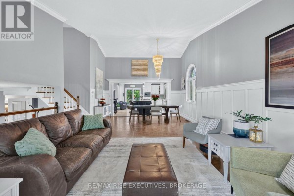 Living room with brown sofa, vaulted ceiling, wainscoting, arched window, and chandelier - 611 Rivermeade Avenue Kingston