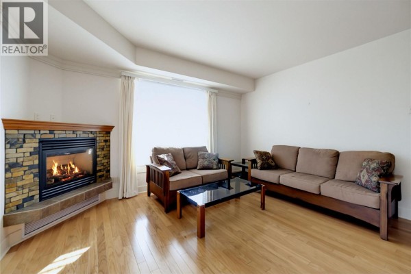 Spacious living room with a gas fireplace, wood flooring, and large windows. - 611 Shuswap Street Sw Unit# 202, Salmon Arm