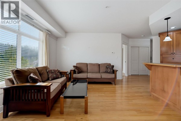 Open-concept living area with wood flooring, two sofas, a coffee table, and a kitchen island. - 611 Shuswap Street Sw Unit# 202, Salmon Arm